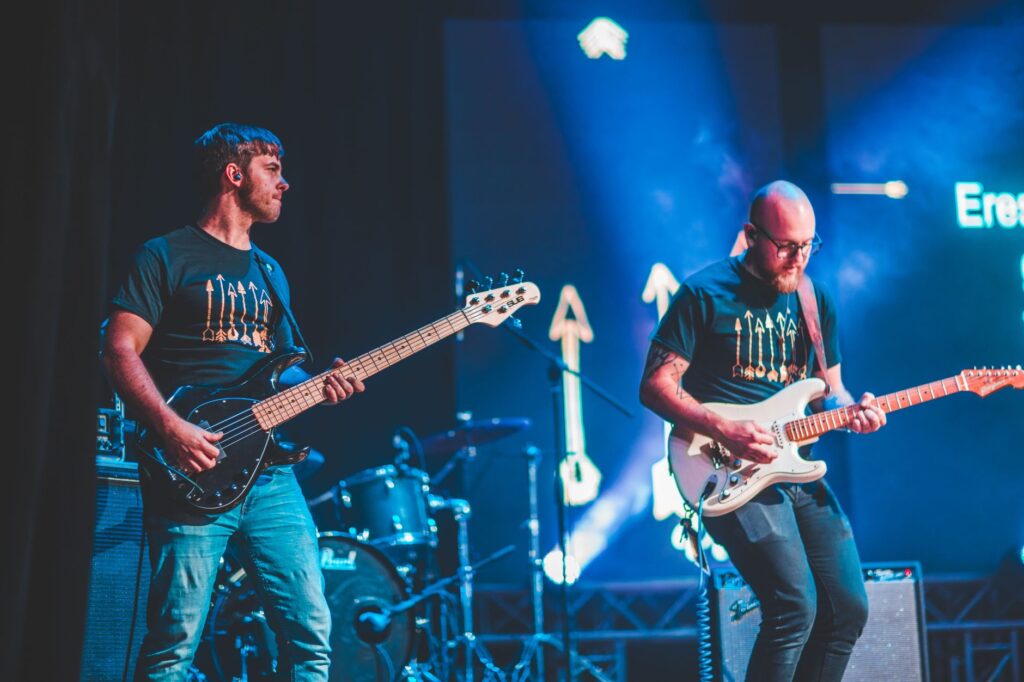 Guitarristas tocando en vivo bajo luces en un escenario, imagen ilustrativa del guitarrista Nick Valensi y Scream Your Name