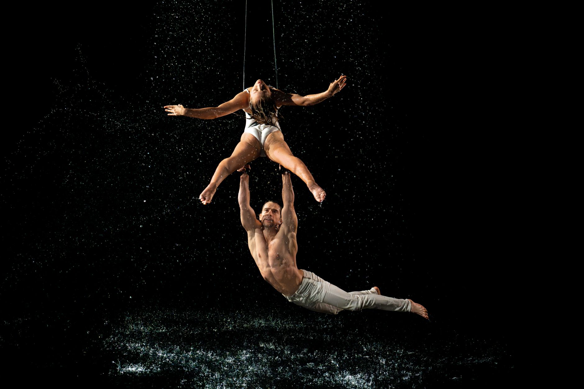 Dos artistas realizan acrobacias aéreas entre salpicaduras de agua, imagen ilustrativa de la lluvia de Magnolias de Rosalía en SNL