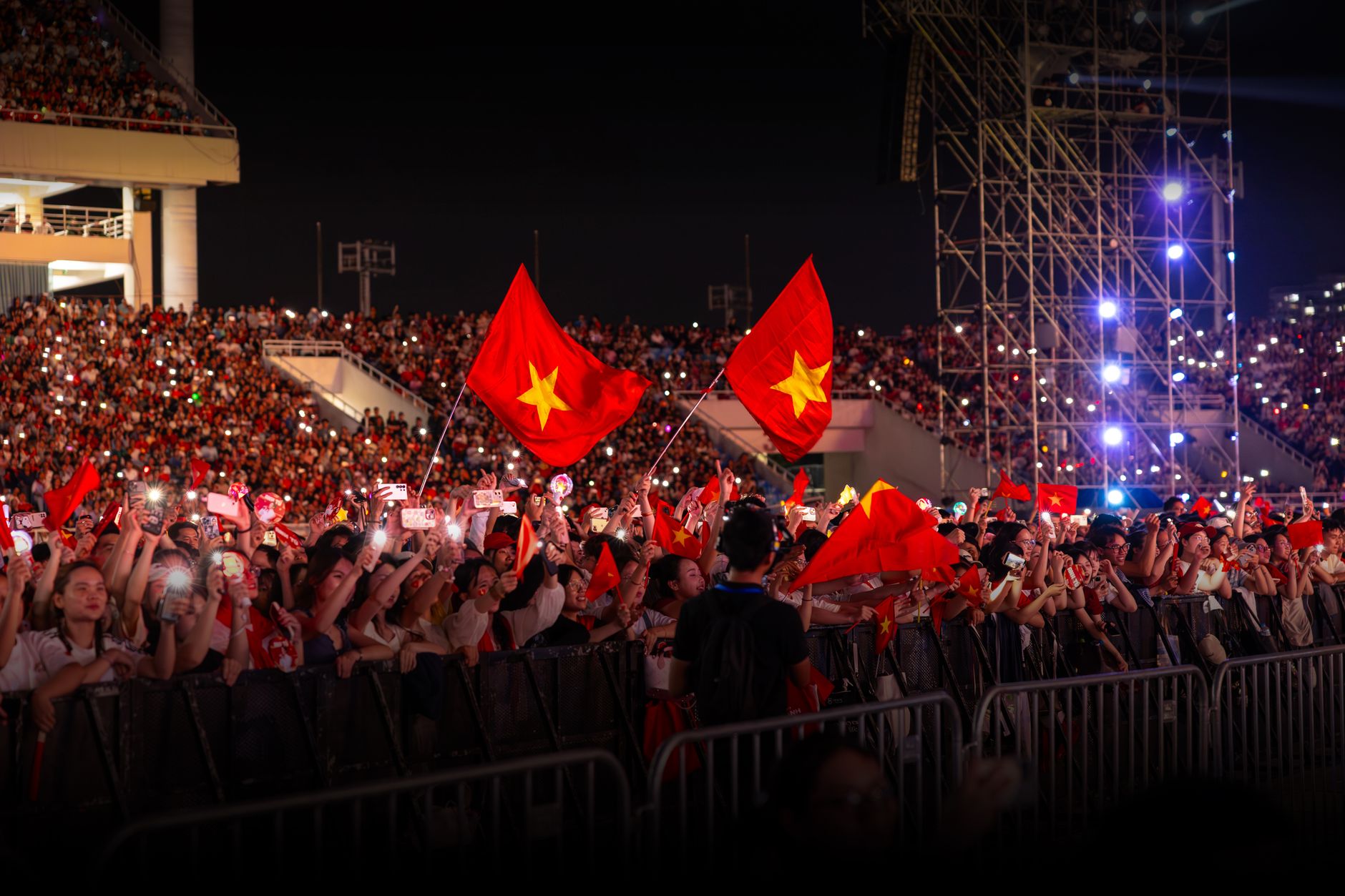Público ondeando banderas en un concierto nocturno bajo luces brillantes, ambiente de la gira de U2